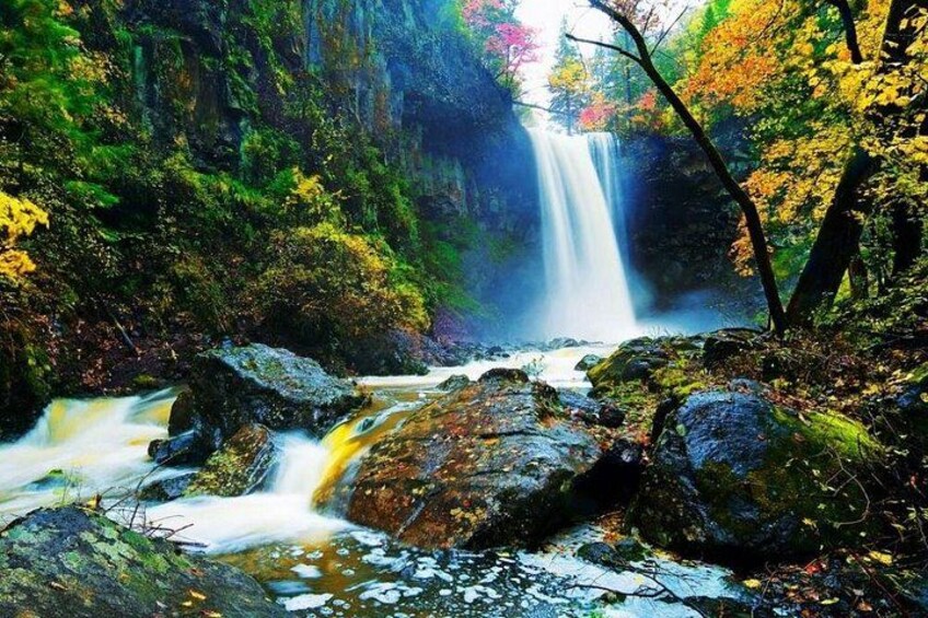 A waterfall in a forested area with rocks and autumn-colored foliage. 3