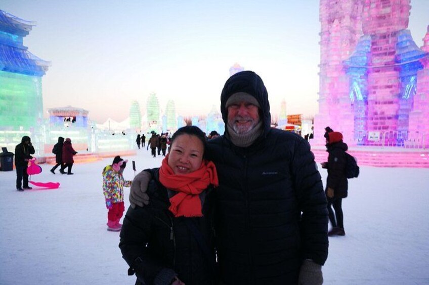 A person and a child in a snowy outdoor setting with illuminated ice sculptures. 1