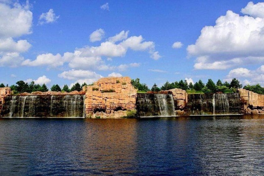 Una cascata che si getta su scogliere rocciose in un bacino d'acqua tranquilla, circondata da alberi e un cielo azzurro limpido. 3