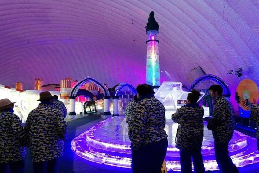 Una pista di pattinaggio sul ghiaccio al coperto con persone che pattinano, strutture illuminate e un pilastro centrale. 5