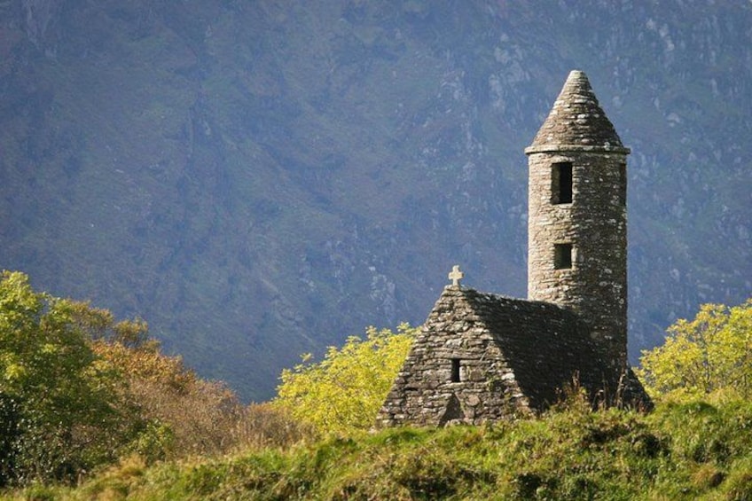 Una torre de piedra con techo cónico, rodeada de vegetación exuberante y montañas al fondo. 2