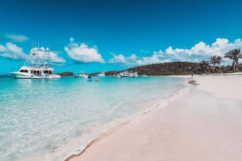 A beach with clear turquoise water, a white sandy shore, and several boats anchored near the shore. 5