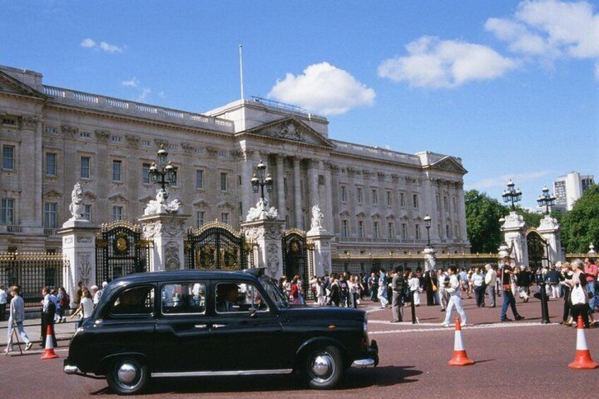 Un coche negro estacionado frente al Palacio de Buckingham, con gente caminando y conos de tráfico naranja. 1