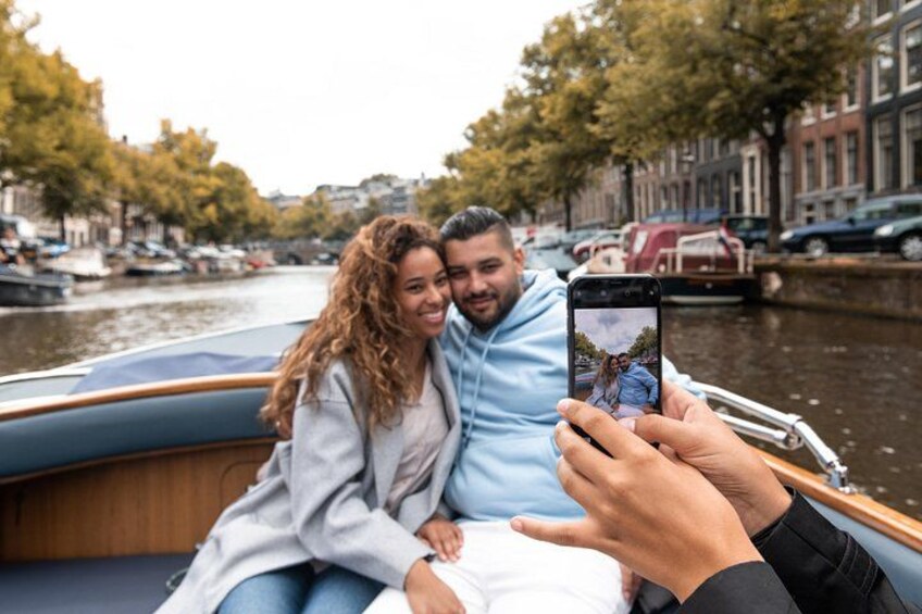 Una pareja en un barco tomándose un selfie con un canal y edificios al fondo. 2