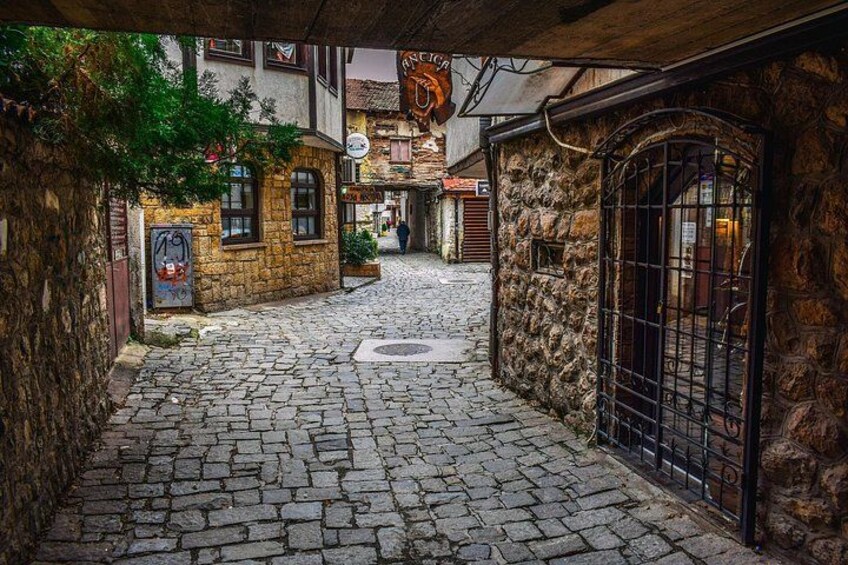 Une rue pavée dans une ville historique, avec des bâtiments en pierre, une porte en métal et une enseigne suspendue. 2