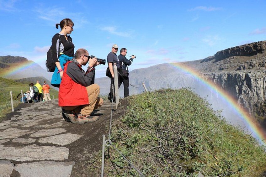 A group of people taking photographs of a rainbow over a canyon. 3
