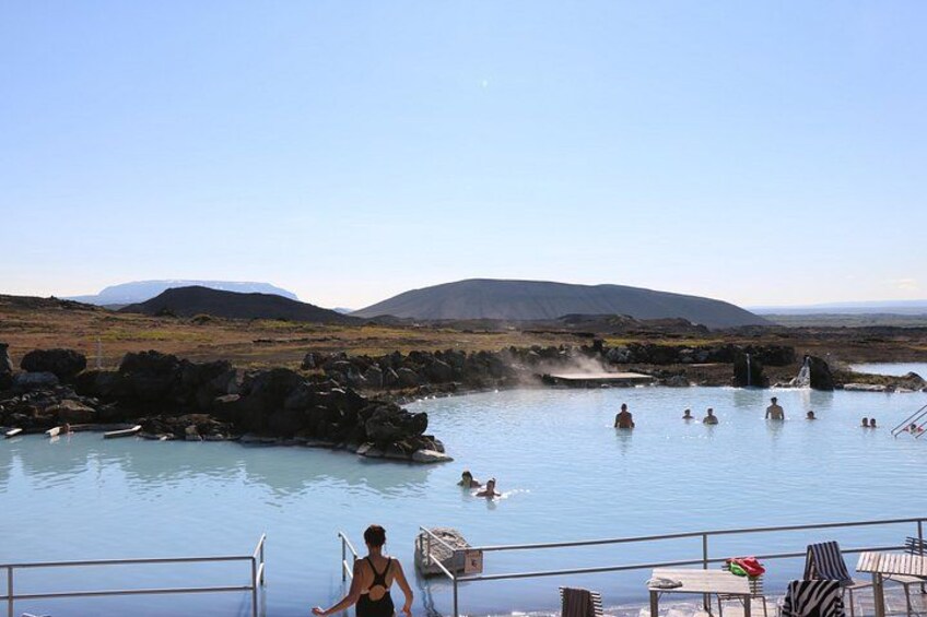 A geothermal spa with people swimming, a rocky landscape, and distant mountains. 1