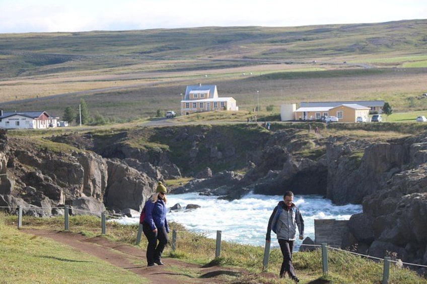 A coastal landscape with a rocky cliff, a path, and a few buildings in the background. 5