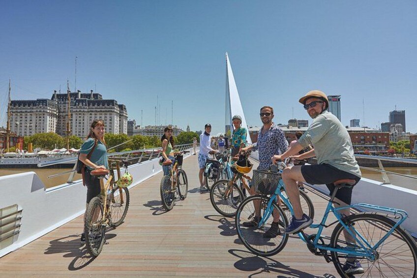 A group of people riding bicycles on a wooden bridge with a cityscape in the background. 4