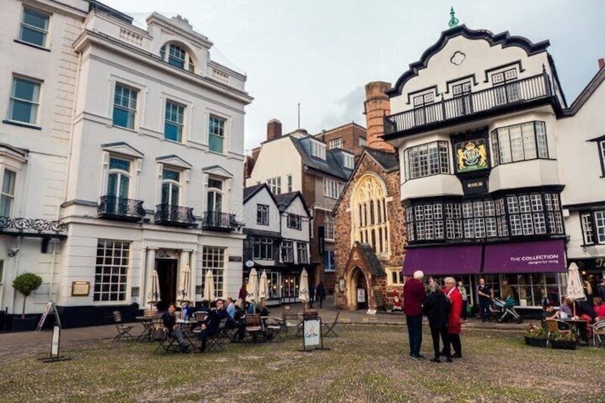 Una calle histórica con arquitectura tradicional, incluyendo un edificio con torre de reloj y otro con letrero de pub. 3