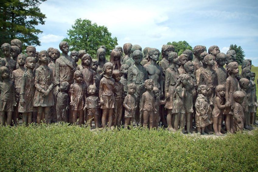 A large group of bronze statues of children and adults in a grassy field. 4