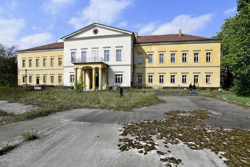 A large yellow building with a central entrance, surrounded by a gravel area with patches of snow. 3