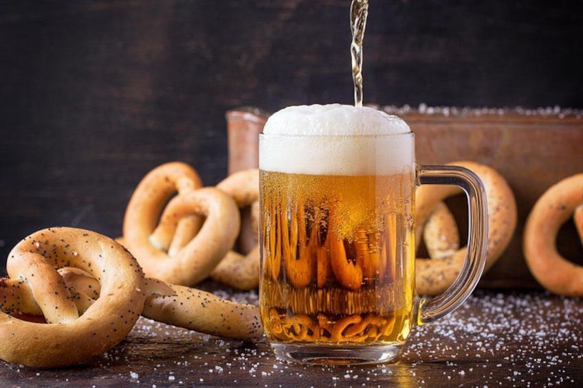 A glass mug of beer with pretzels and salt scattered around. 2