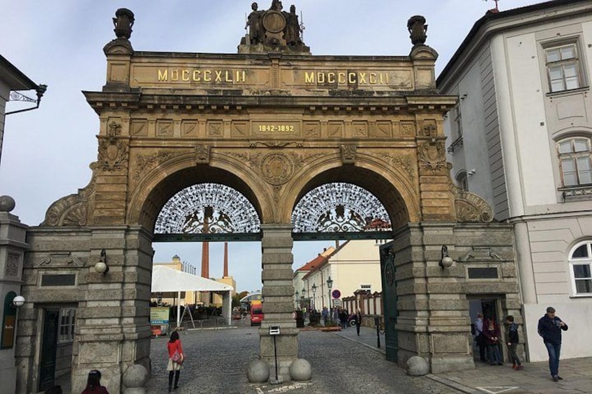 An ornate stone archway with inscriptions and decorative elements, leading to a building with a tiled facade. 5
