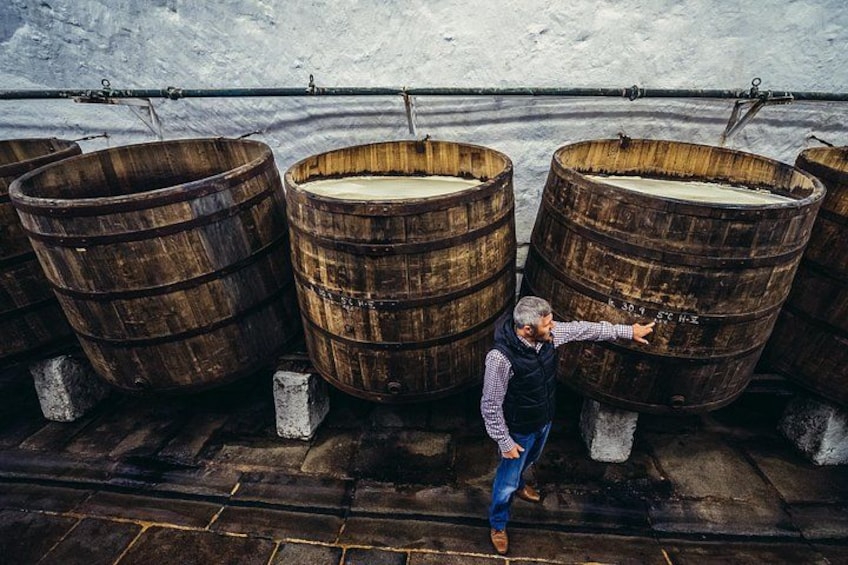 A man standing between large wooden barrels, pointing at one of them. 3