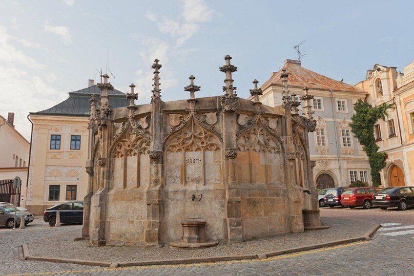 Una estructura histórica de piedra con detalles labrados, rodeada de calles empedradas y edificios clásicos. 1
