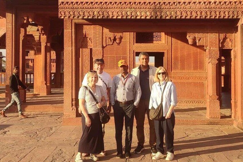 A group of people standing in front of a red sandstone structure with intricate carvings. 1