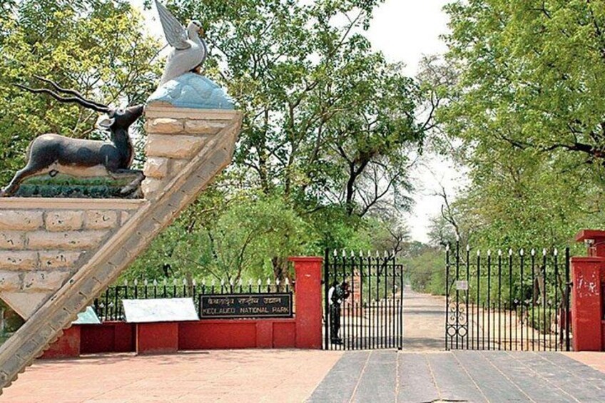 A park entrance with a gate, a statue of a bird and a deer, and a sign that reads 'Kheda National Park'. 4