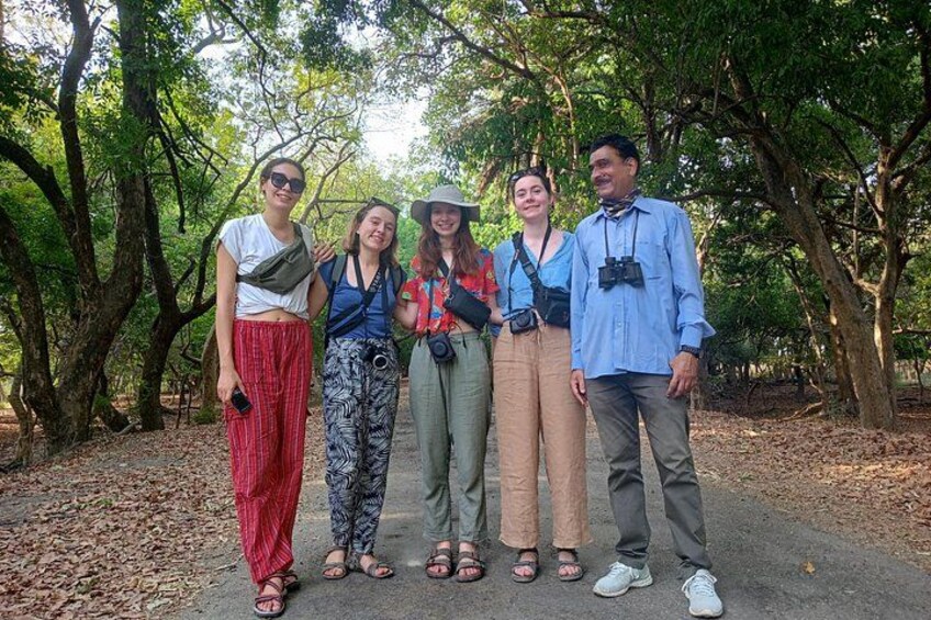 A group of people standing in a forested area with trees and a dirt path. 1
