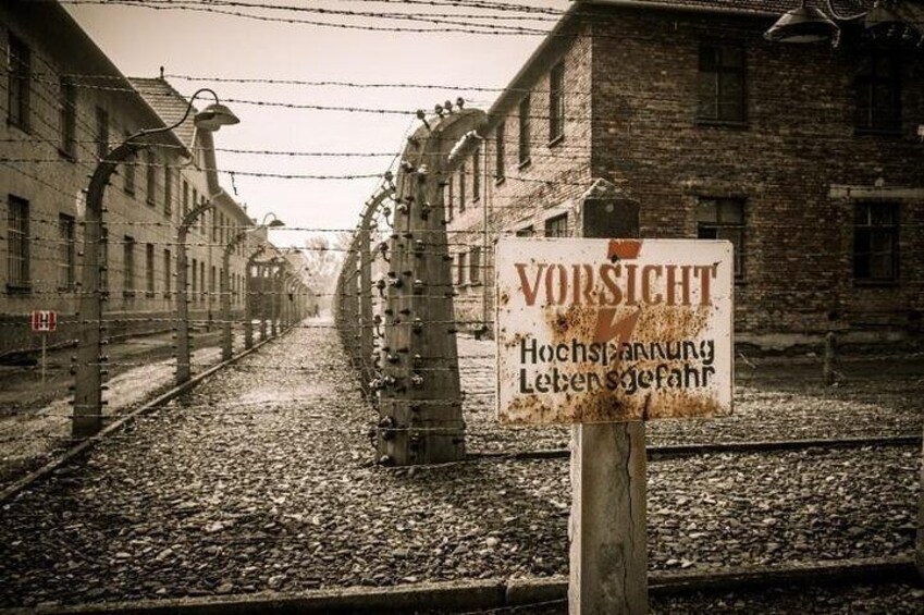 A railway track with barbed wire fences and a sign reading "VORSICHT Hochspannung Leben gefährlich". 1