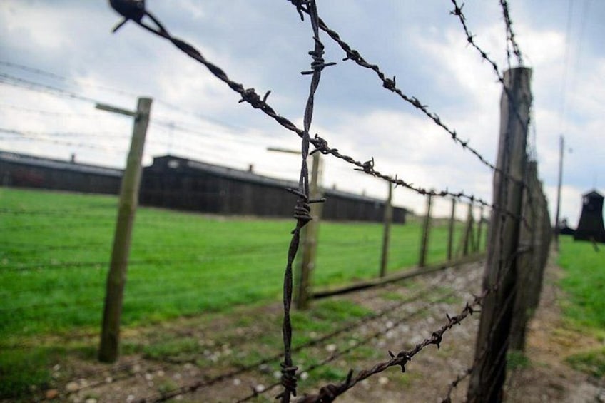 A barbed wire fence with a grassy field and a building in the background. 1