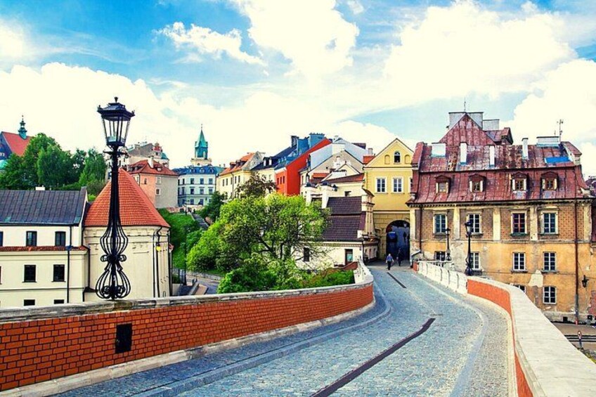 A cobblestone street in a historic town with old buildings, a red brick wall, and a street lamp. 2