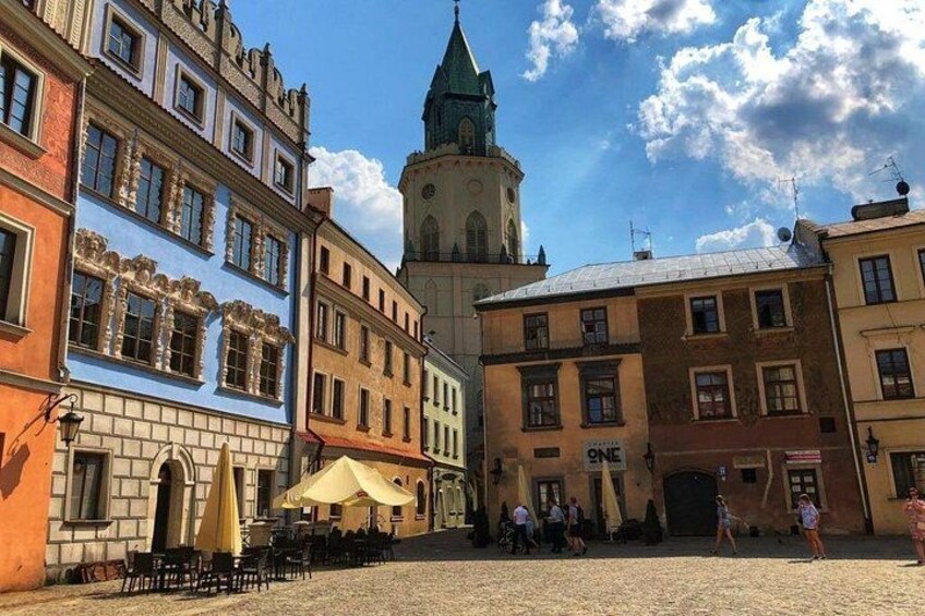 A cobblestone square with colorful buildings, a clock tower, and outdoor seating. 5