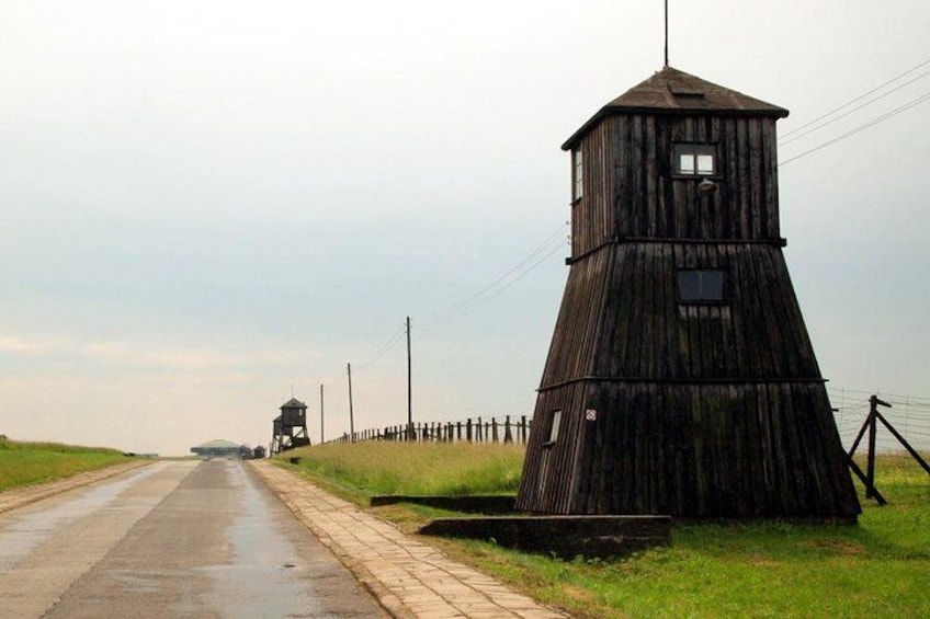 Ein hölzerner Aussichtsturm an einer Straße mit Zaun und einem kleinen Gebäude in der Ferne. 2