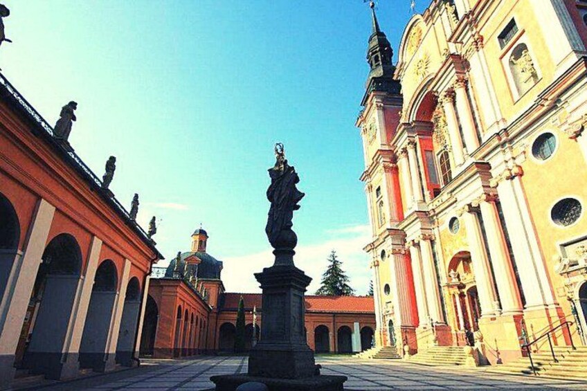 A courtyard with a statue, red buildings, and a church with a dome. 4