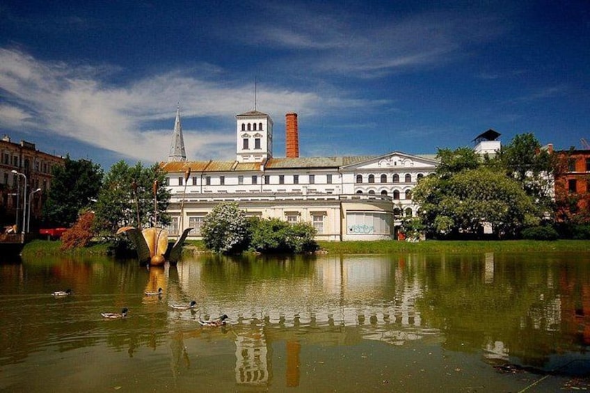 Un edificio histórico con una torre, un estanque con patos y un cielo azul despejado. 1