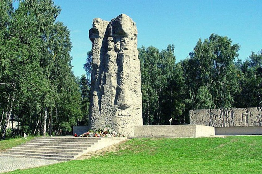 A large stone monument with carved figures, surrounded by a grassy area and trees. 4
