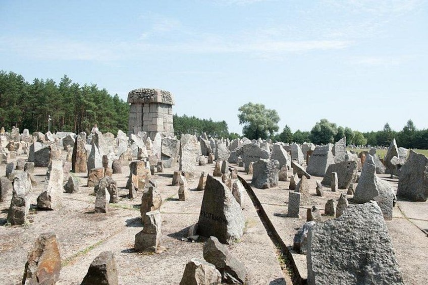 A field of upright stone structures, a central stone tower, and a forested background. 1