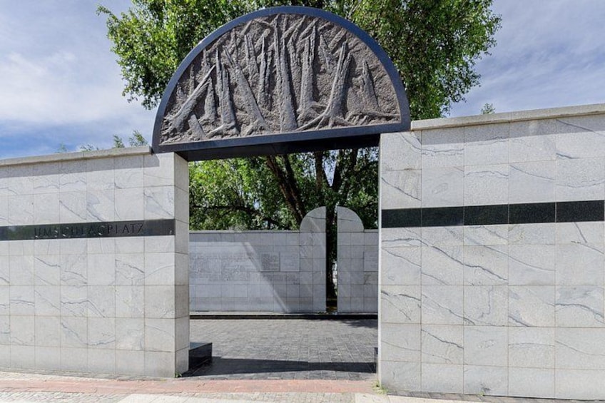 A stone archway with a relief sculpture, a tiled wall, and a tree in the background. 3