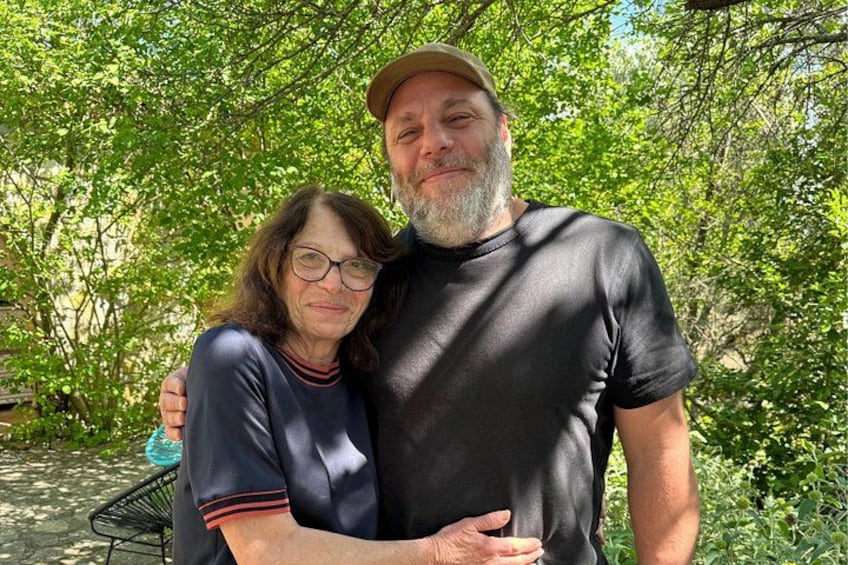 Two people standing outdoors with trees in the background. 3