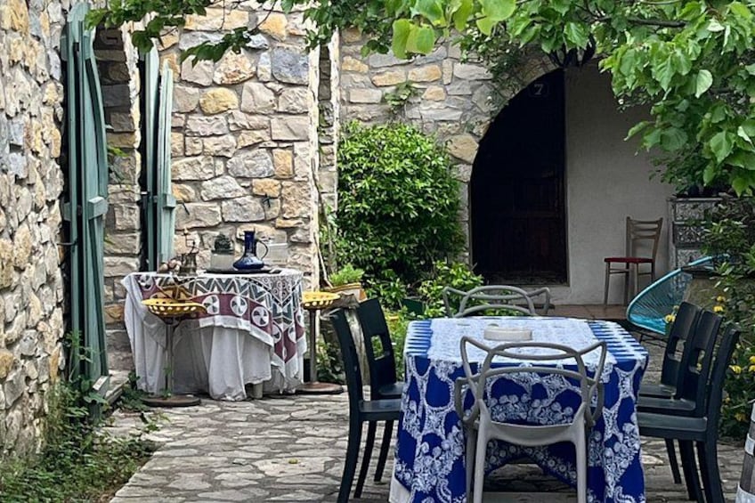 An outdoor dining area with stone walls, a table with a blue and white tablecloth, and chairs. 2