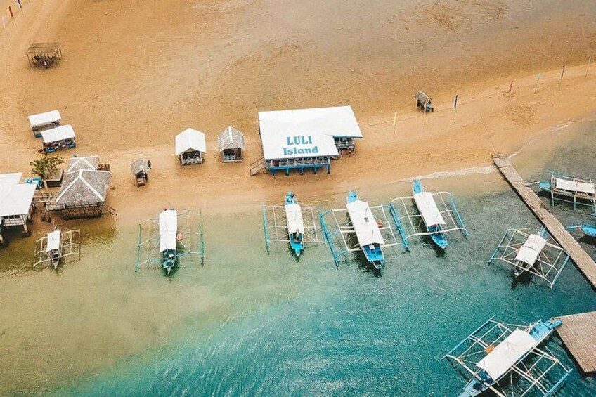 En strand med en flydende konstruktion kaldet 'LULI Island', flere både fortøjet ved kajen og en sandet kystlinje. 5