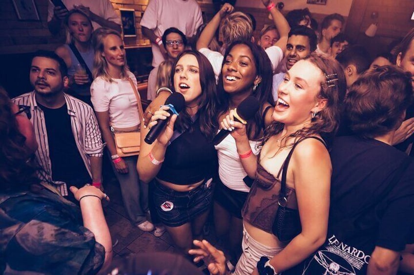Een groep mensen bij een feest, sommigen met microfoons, wat wijst op een karaoke- of zangactiviteit. 3