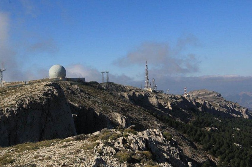 Een bergachtig landschap met een grote bolvormige structuur, mogelijk een radar of weerstation, en verschillende communicatietorens. 3