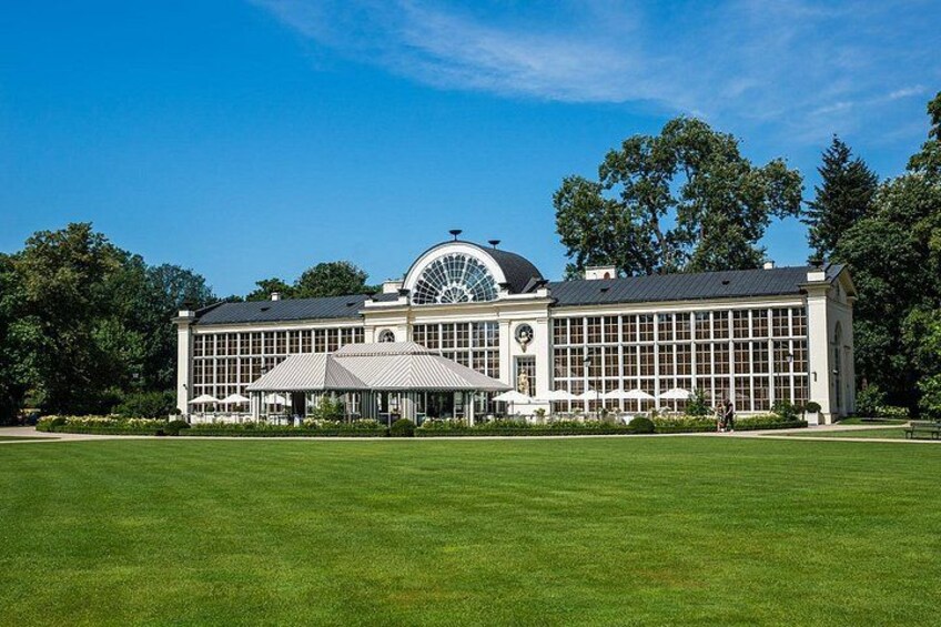 A large, historic building with a dome and extensive windows, surrounded by a well-maintained lawn and trees. 1