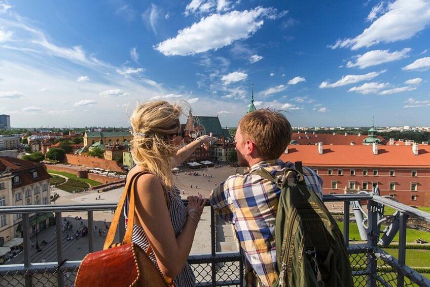 A couple overlooking a cityscape with a prominent tower and red-roofed buildings. 3