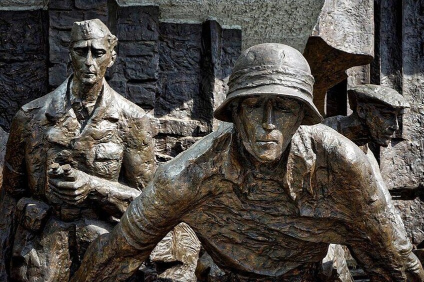 Bronze statues of soldiers in uniform, set against a stone wall backdrop. 5