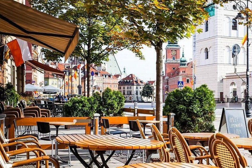 Outdoor seating with tables and chairs, a street with buildings, and a clock tower in the background. 1