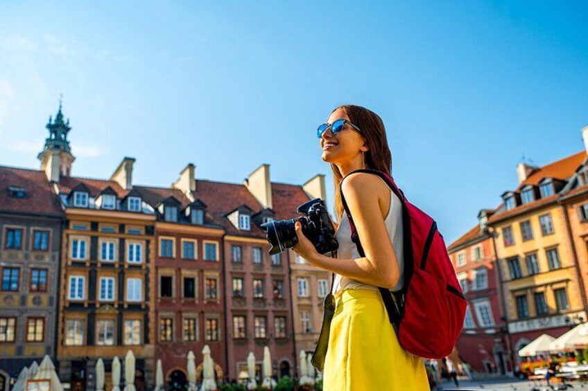 A person with a camera and a red backpack in a historic town square with old buildings. 2