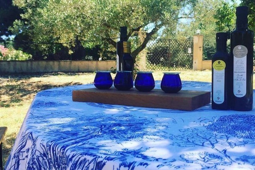 A table with a blue tablecloth, four blue cups, and two bottles of olive oil. 1