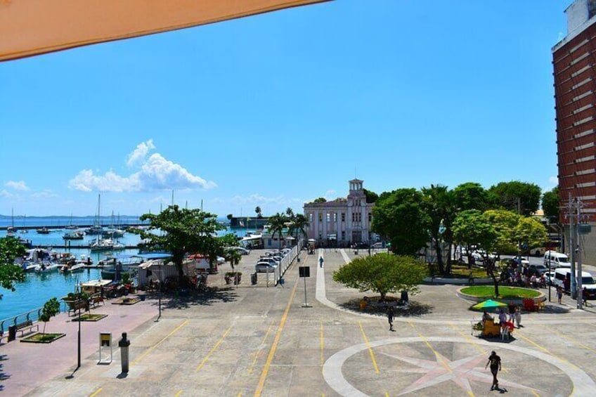 A marina with boats, a large building, and a pedestrian area with trees and benches. 2