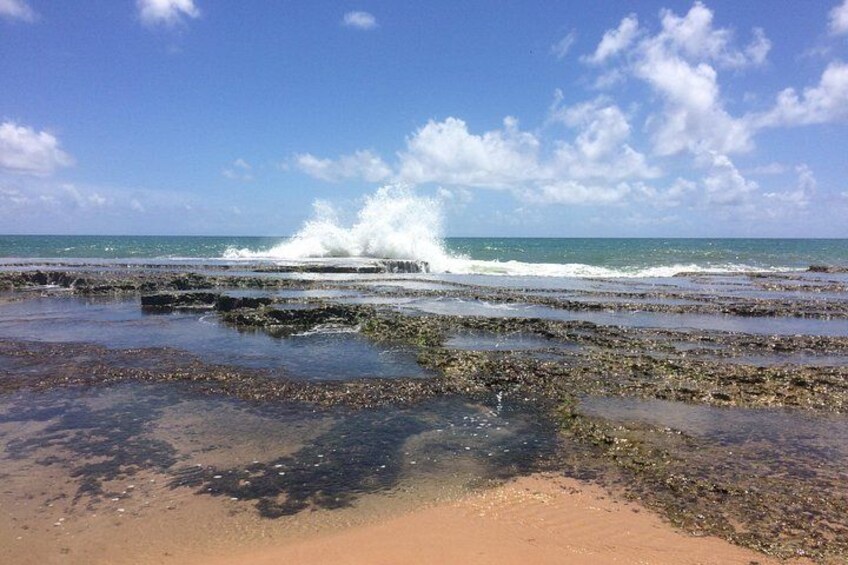 A beach with waves crashing onto rocks and a clear sky. 5