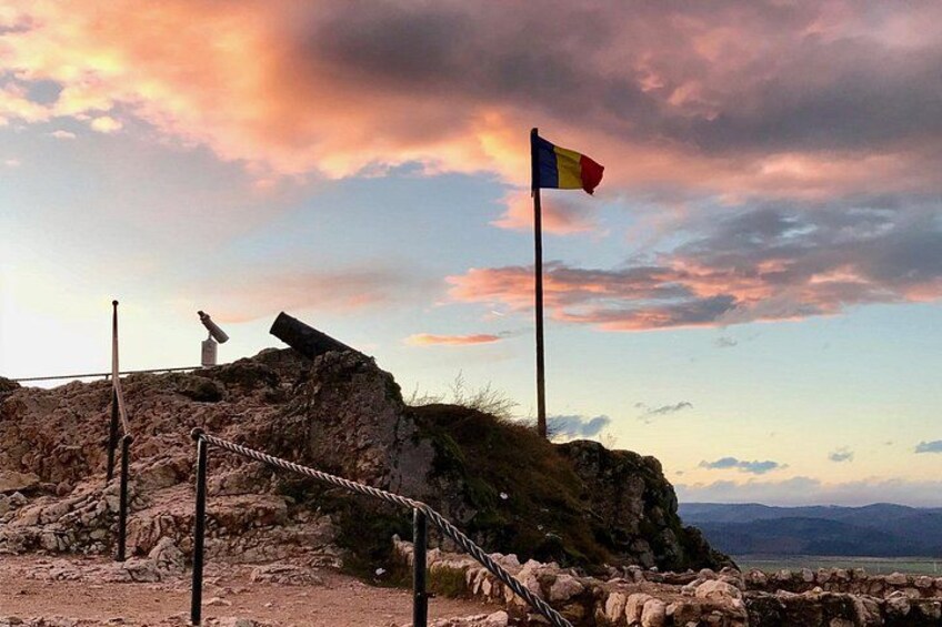 A rocky landscape with a flagpole and a flag, a rope barrier, and a sunset sky. 5