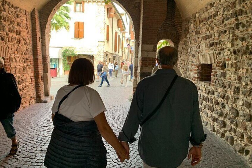 A cobblestone street with stone walls, people walking, and a building with a window in the background. 4