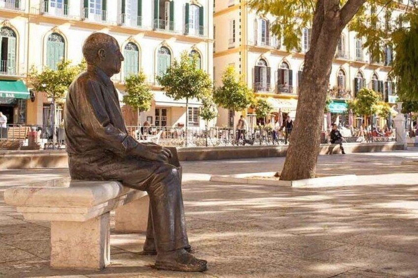 Una statua in bronzo raffigura un uomo seduto in una piazza pubblica, sullo sfondo edifici. 3