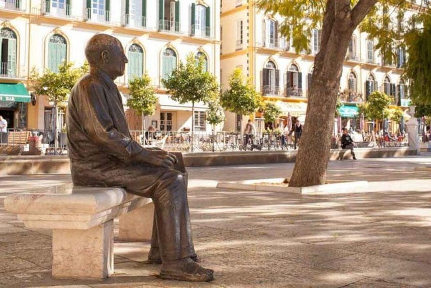 A bronze statue of a seated man in a public square with buildings in the background. 2